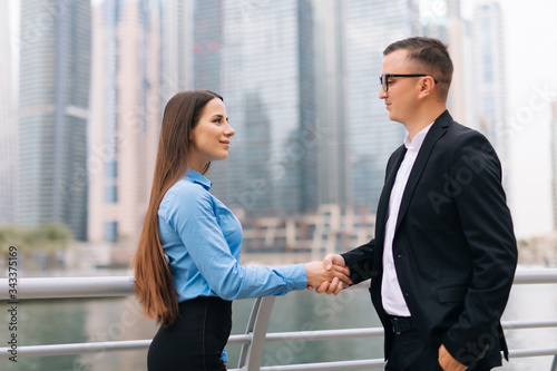 An attractive business man and woman team shaking hands outdoors on skyscrapers