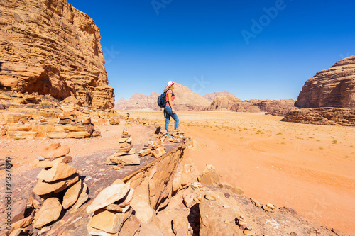 Woman with backpack and hat looking on desert from rock. Wadi Rum, Jordan. Travel and tourism concept.