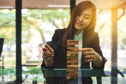 An asian woman build Tumble tower wooden blocks for management and strategy in business concepts