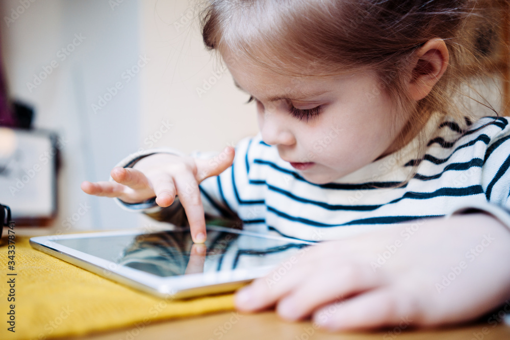 Pretty little girl playing kid's application using wireless tablet computer. Toddler growing with gadget in cozy place Pretty little girl playing kid's application using wireless tablet computer. Toddler growing with gadget in cozy place