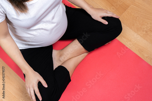 top view of pregnant young woman with white t-shirt and black pants sitting on a yoga mat