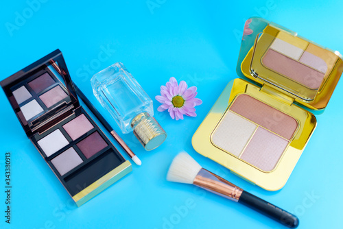 premium makeup brushes, bottle of perfume and blush pads on a bright blue background, creative cosmetics flat lay