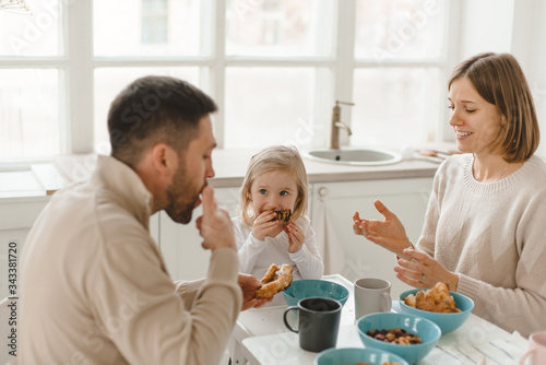 Young cute family with little daughter have breakfast at home in the kitchen.