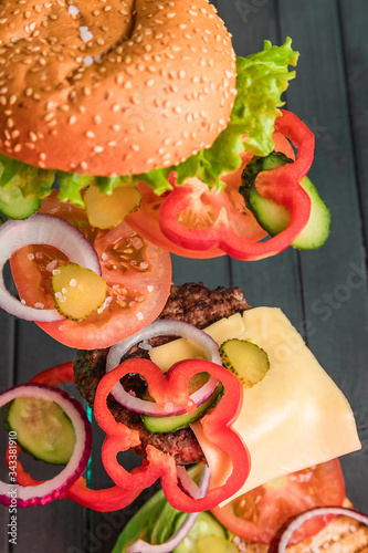 Fototapeta Naklejka Na Ścianę i Meble -  A delicious homemade Burger. The ingredients of a juicy Burger hover over a wooden table. Food against the dark boards. Meat, cheese, vegetables and rolls.