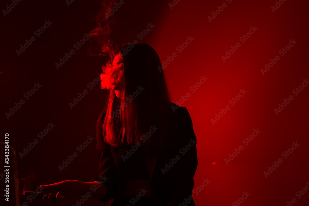 Girl model smokes vape in red light. Girl model smokes vape in red light.