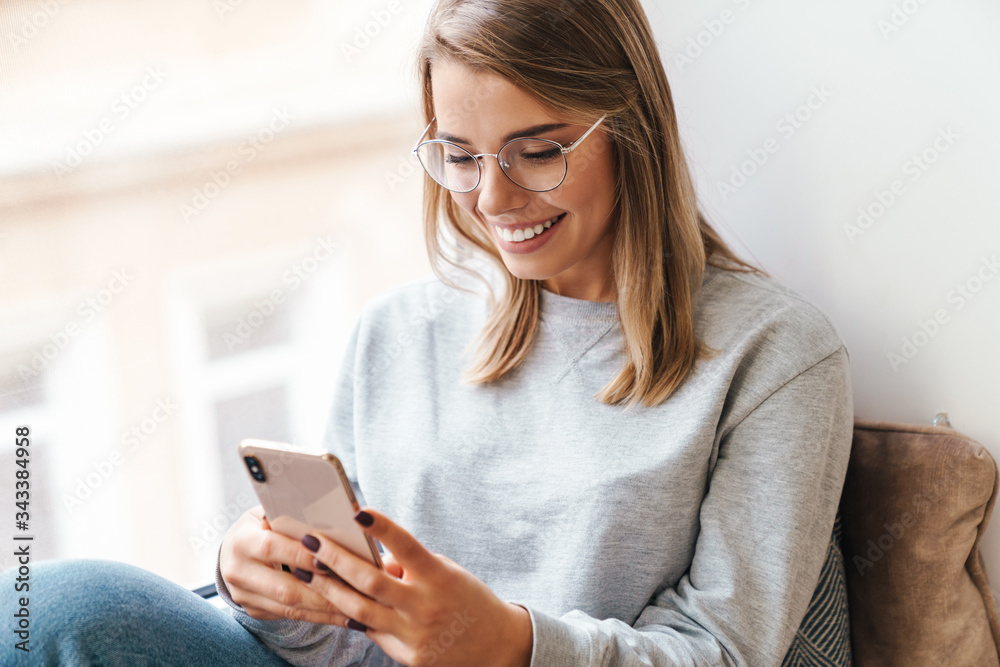 Photo of smiling woman using smartphone while sitting near window Photo of smiling woman using smartphone while sitting near window