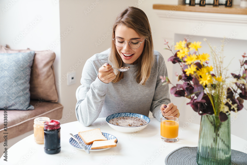 Photo of cheerful young woman eating cereal while having breakfast Photo of cheerful young woman eating cereal while having breakfast