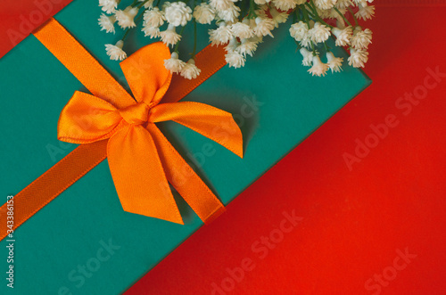 Gift with ribbon and white flowers lie on red background top view copy space