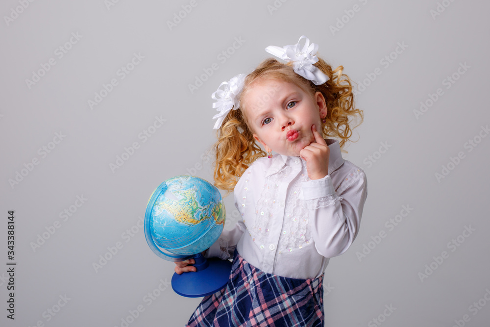 a small curly haired blonde girl in a school uniform holds a globe in her hands thinking on a white background a small curly haired blonde girl in a school uniform holds a globe in her hands thinking on a white background