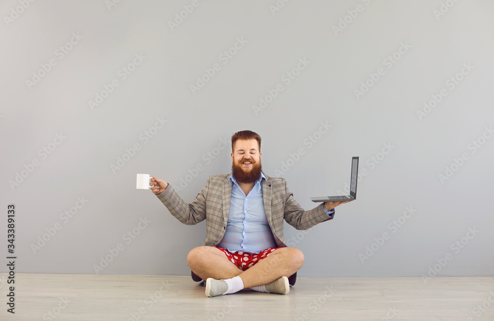 Funny fat bearded man in a jacket and red shorts with a laptop on a gray background.Freelancer online distance work concept. - obrazy, fototapety, plakaty 