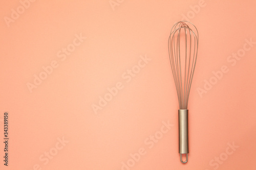 Metal whisk for whipping on a rosa background.