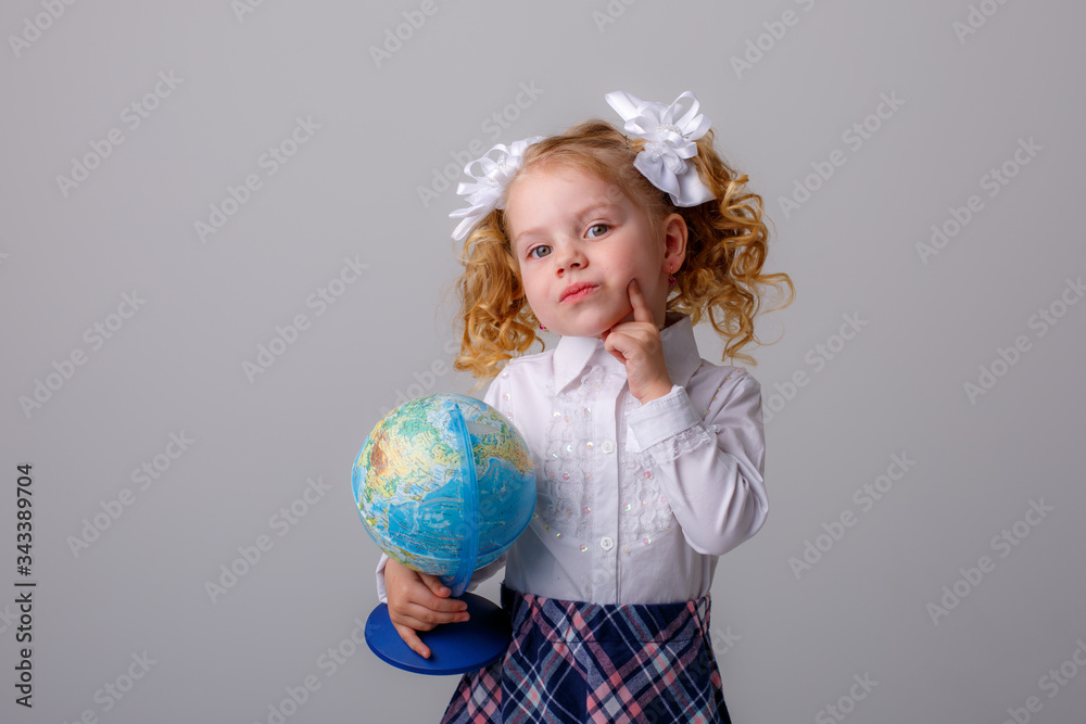 a small curly haired blonde girl in a school uniform holds a globe in her hands thinking on a white background a small curly haired blonde girl in a school uniform holds a globe in her hands thinking on a white background