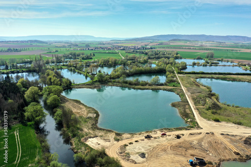 Aerial view of an active gravel pond beside the river Leine near Sarstedt, Germany, with a truck and piles of sand and a village in the background