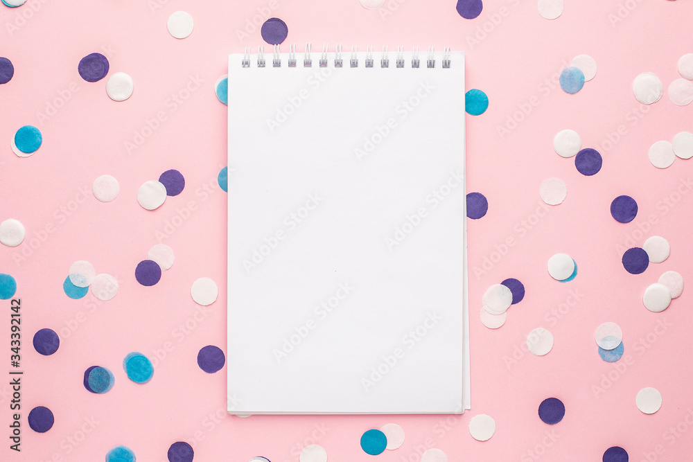 Notebook and blue, white and lilac confetti on pink color paper background minimal style
