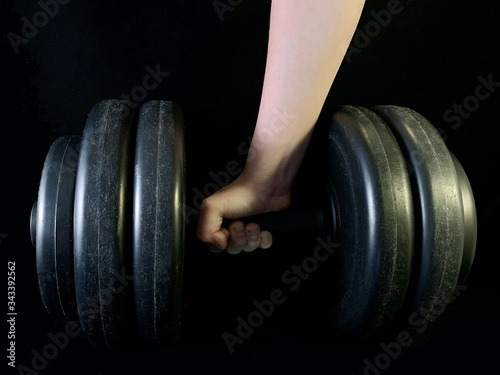 Hand with a heavy dumbbell on a black background. Pancake dumbbell for bodybuilding.
