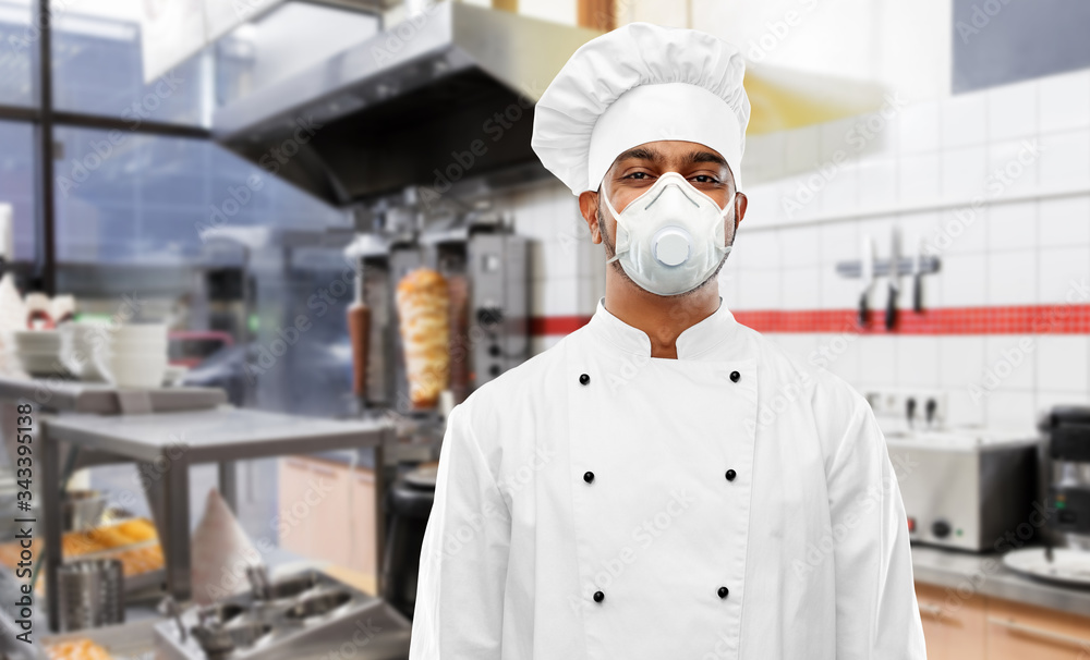 health protection, safety and pandemic concept - indian male chef cook wearing face protective mask or respirator over kebab shop kitchen background