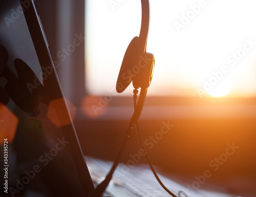 Headphones with a microphone hang on a laptop at home against the backdrop of a sunny sunset. The concept of remote work at home during the coronavirus, copy space, quarantine © HENADZY