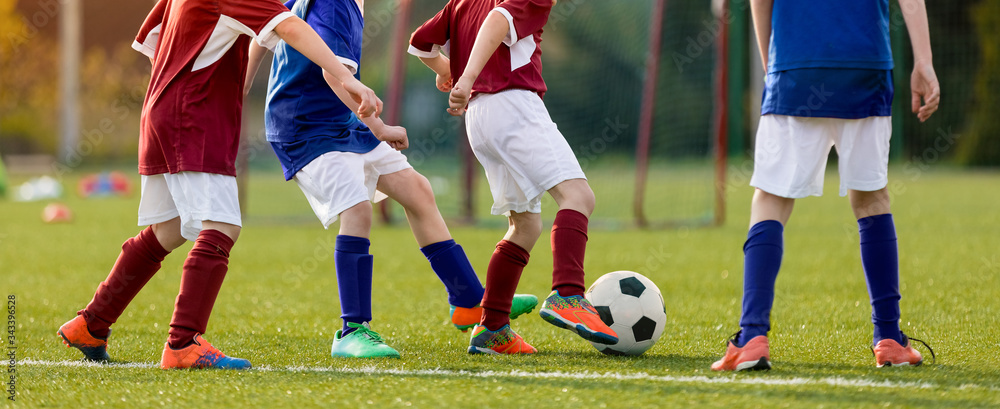 Children practicing football on grass lawn. Elementary age kids kicking soccer ball on primary school pitch. Boys between the ages of 6–11 playing sports Children practicing football on grass lawn. Elementary age kids kicking soccer ball on primary school pitch. Boys between the ages of 6–11 playing sports
