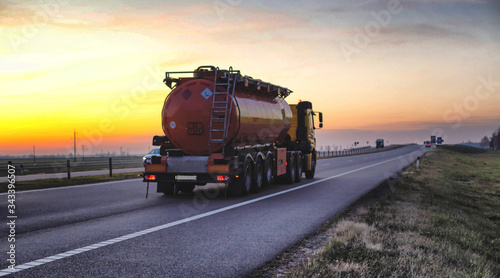 A truck carries a tank of combustible fuel on a highway against a forest and blue sky. The concept of transportation of dangerous goods on the road, license, sunset photo