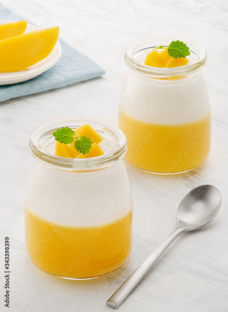 Sweet dessert of yogurt and mango with mint. Two jars with dessert on a light table Sweet dessert of yogurt and mango with mint. Two jars with dessert on a light table