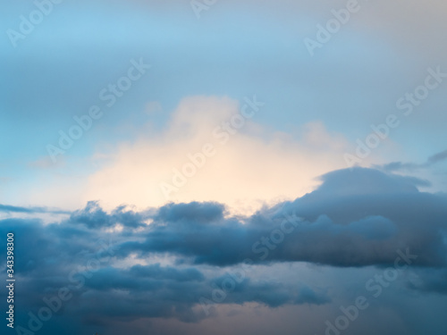 dark clouds in front of white sunlit cloud in blue sky at spring dusk