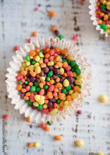 multicolored small candies in paper cupcakes on wooden background. Festive and birthday concept