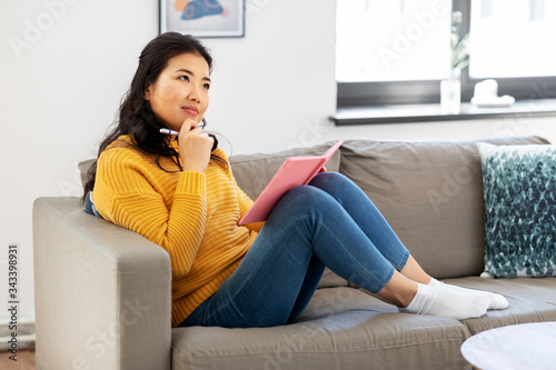 Free Download people and leisure concept - thinking asian young woman with diary or notebook sitting on sofa at home - GFXLoad