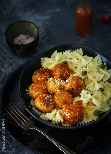Farfalle pasta with chicken meatballs in tomato sauce, on a dark background
