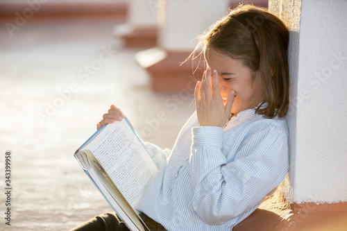Photography Little girl laughing a lot reading a book sitting on the rooftop