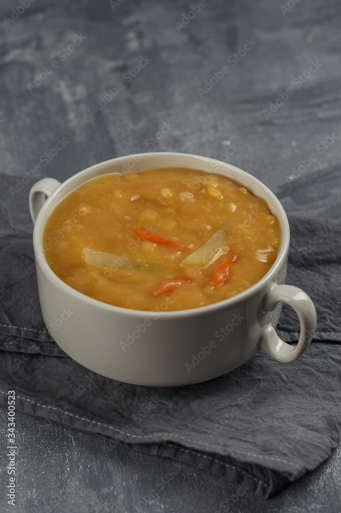Split pea soup with sliced potato and carrot. Vegetarian vegetable pea soup in white bowl on grey background. Split pea soup with sliced potato and carrot. Vegetarian vegetable pea soup in white bowl on grey background.