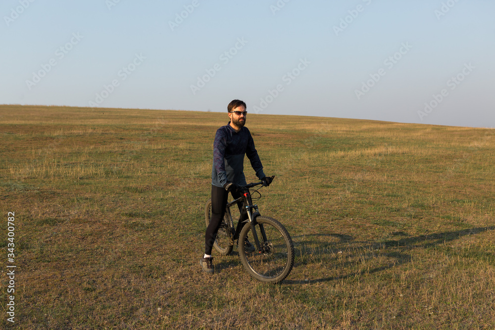 Cyclist in shorts and jersey on a modern carbon hardtail bike with an air suspension fork standing on a cliff against the background of fresh green spring forest Cyclist in shorts and jersey on a modern carbon hardtail bike with an air suspension fork standing on a cliff against the background of fresh green spring forest