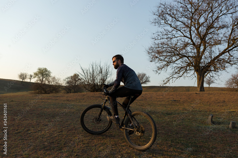 Cyclist in shorts and jersey on a modern carbon hardtail bike with an air suspension fork standing on a cliff against the background of fresh green spring forest Cyclist in shorts and jersey on a modern carbon hardtail bike with an air suspension fork standing on a cliff against the background of fresh green spring forest