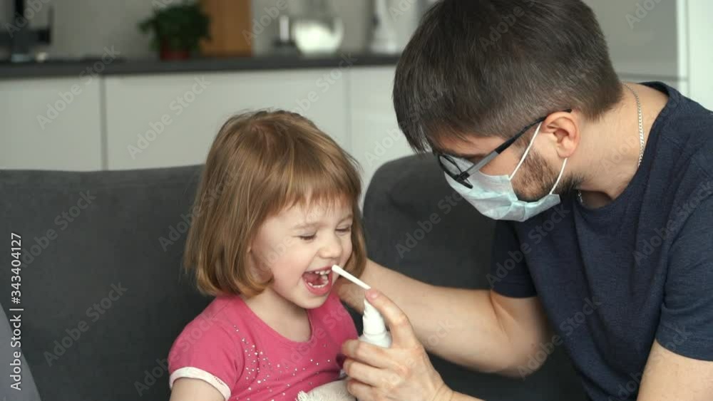 Portrait of young father sanitizes mouth his little funny 3 years old daughter with disinfecting antiseptic spray. Concept of disinfection against Viruses and Bacteriaю. Prevention against Coronovirus Portrait of young father sanitizes mouth his little funny 3 years old daughter with disinfecting antiseptic spray. Concept of disinfection against Viruses and Bacteriaю. Prevention against Coronovirus
