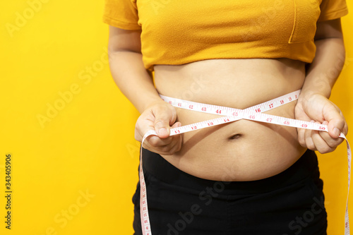 fat woman check out body overweight abdomen she belly with in hand measuring tape for yellow or obesity background. Weight loss concept. photo
