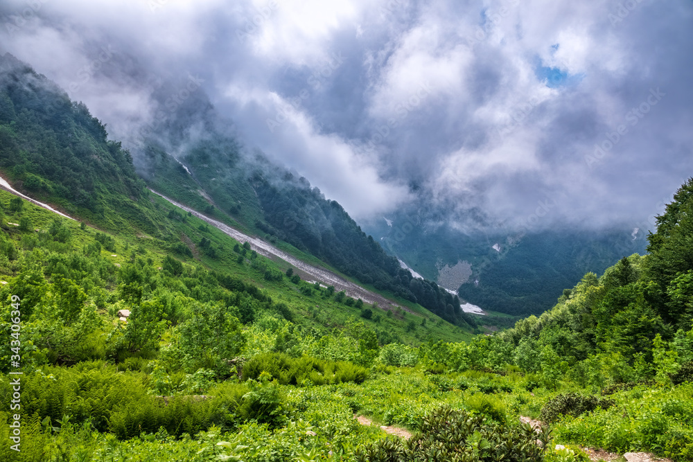 Fototapeta premium The green slopes of high mountains are hidden in clouds and fog. Melting snow in high mountains.