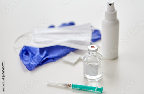 medicine and healthcare concept - close up of syringe, drug, wound wipes, hand sanitizer with gloves and mask on table