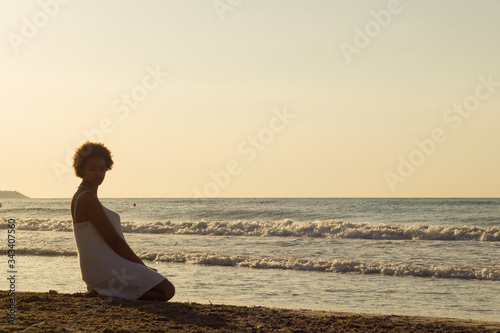 African American black woman thinking on the beach in the sunrise with white dress.