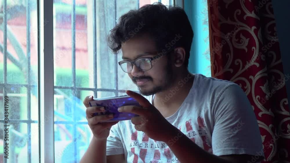 Bored alone Asian male playing games in mobile at home due to Covid-19 Coronavirus Lockdown, self isolation and social distancing
