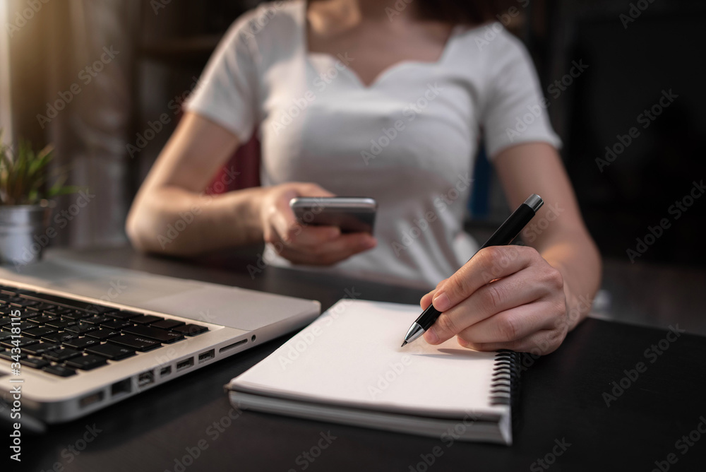 Female businessman use smartphone and take notes in the notebook at the office desk in the morning. Female businessman use smartphone and take notes in the notebook at the office desk in the morning.