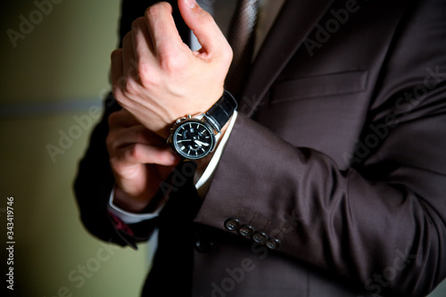 One young man puts a black watch on his wrist. A man in a black suit in a dark room.