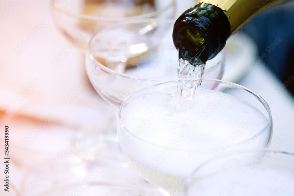 Champagne is poured into a white transparent glass from a bottle. On a Sunny festive summer day, glasses sparkle in the sun.