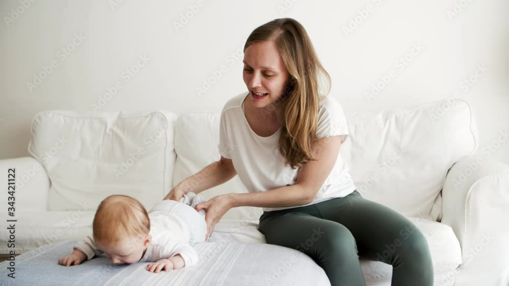 Cheerful mom training baby daughter to turn from belly to back. New mother nursing six month child at home. Baby care and parenthood concept Cheerful mom training baby daughter to turn from belly to back. New mother nursing six month child at home. Baby care and parenthood concept
