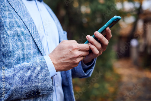 Close-up picture of groom's hands, holding phone. Wedding organization process.