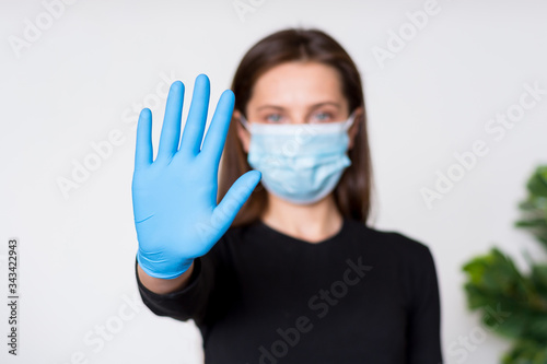 Young woman in medical mask and gloves shows stop sign by her hand.
