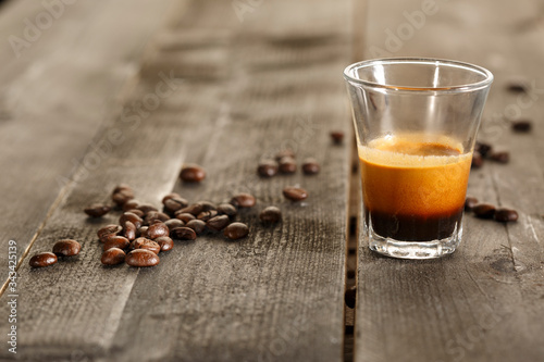 tazzina di caffè in vetro con dei chicchi sopra delle tavole di legno photo