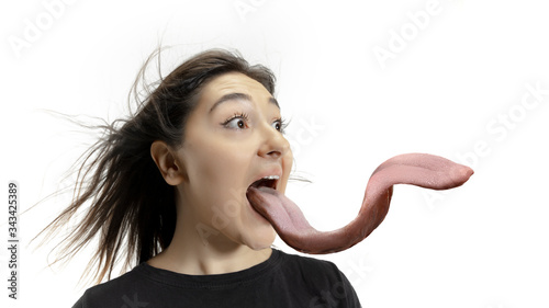 Slika na platnu Smiling girl opening her mouth and showing the long big giant tongue isolated on white background