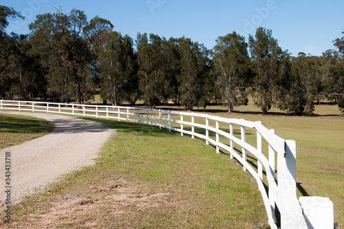 Mogo Australia, view along white wooden fence and dirt road with farm paddock in background