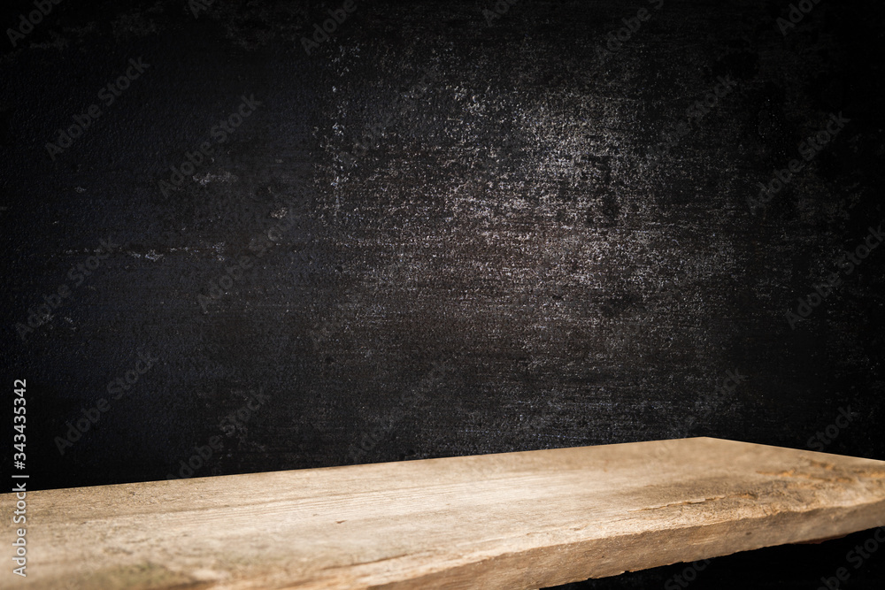 Old wooden table top with a dirty concrete block wall in a dark room background. Old wooden table top with a dirty concrete block wall in a dark room background.