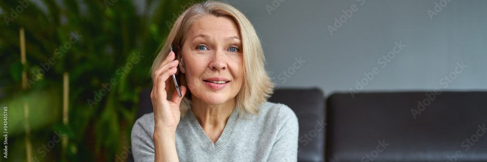 Happy mature woman using mobile phone while sitting on sofa at home Happy mature woman using mobile phone while sitting on sofa at home