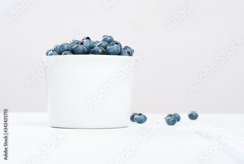 bilberry fruits at white ceramic cup, on bright wood table photo